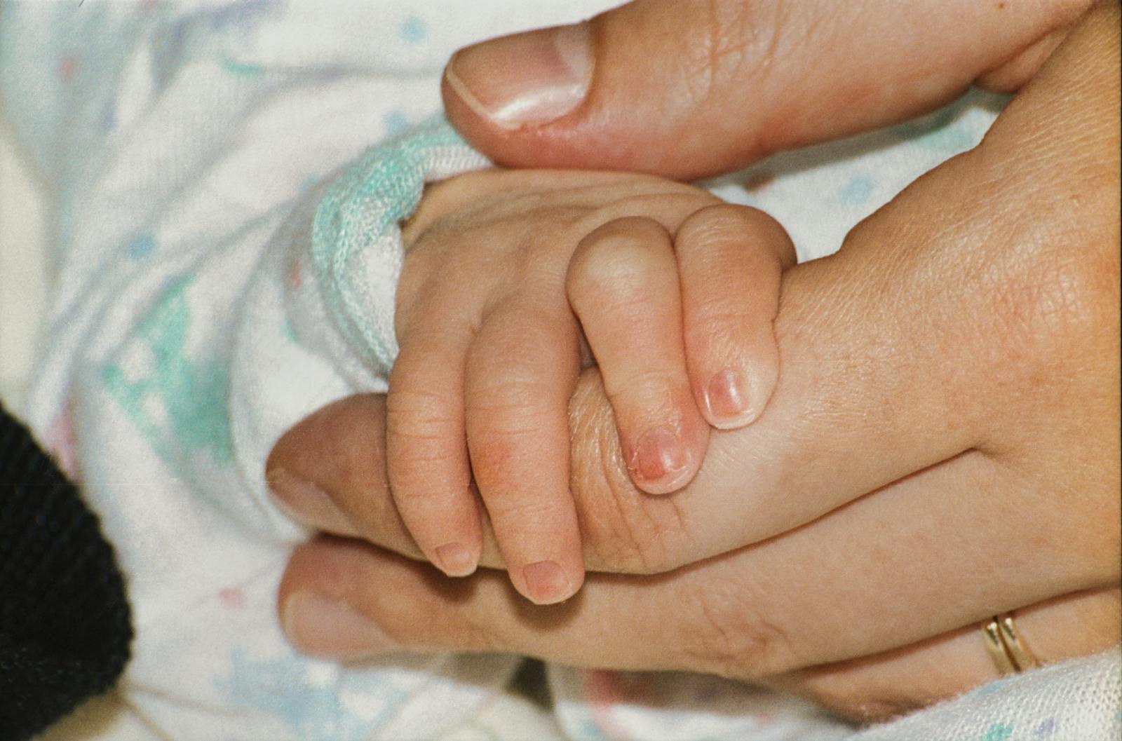 Newborn baby holding an adult's finger with a tiny hand