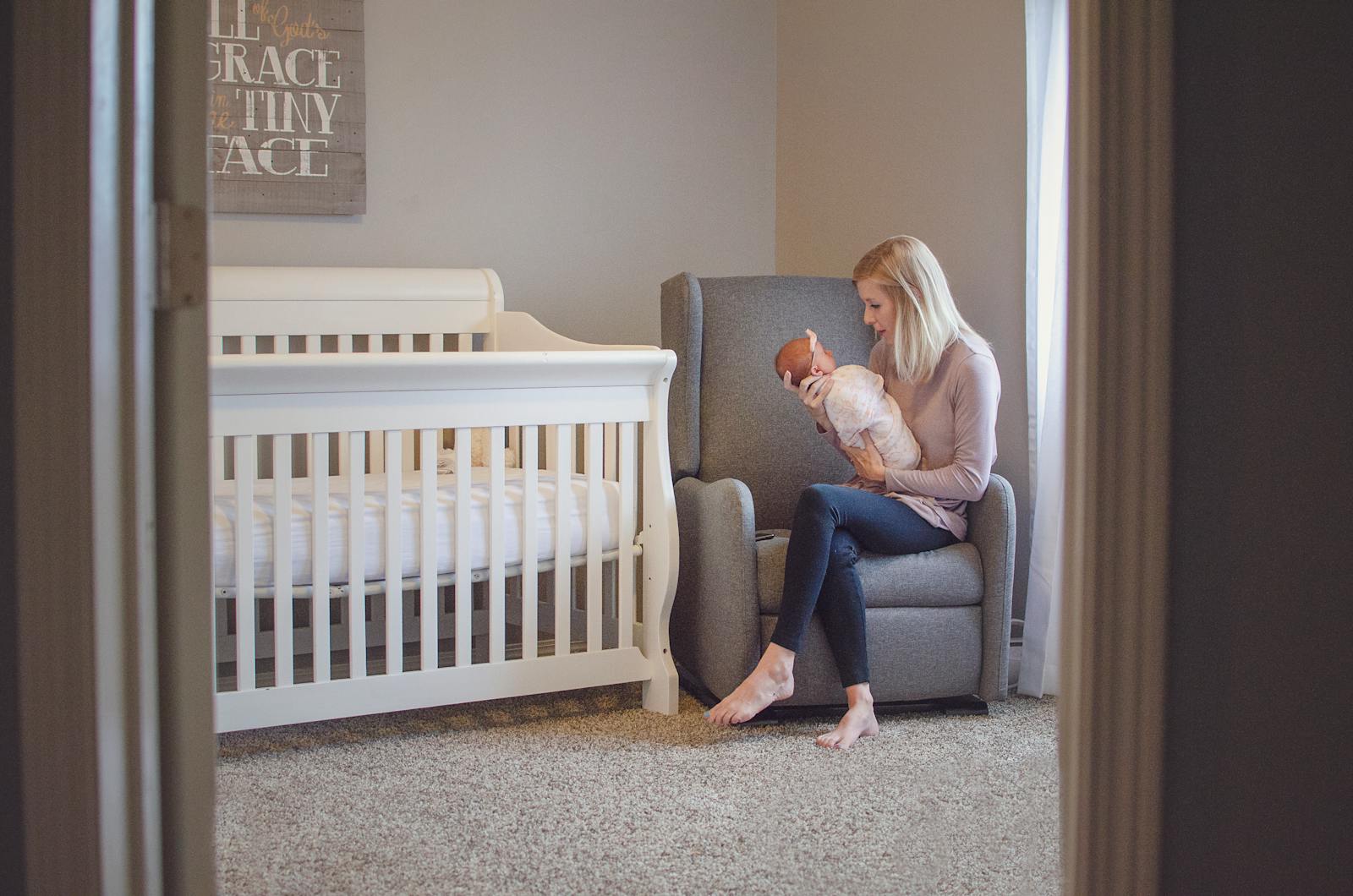 Mother in a nursery chair holding her newborn baby in a warm, quiet setting